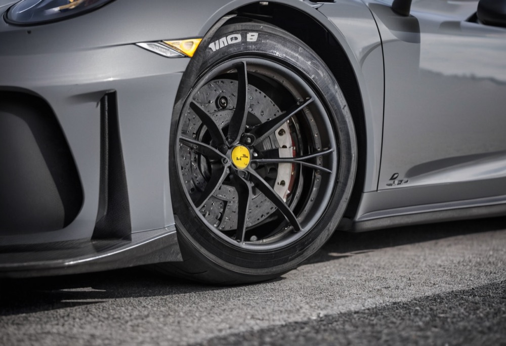 Low close-up of a GT3 car's front wheel, carbon splitter and slick racing tyre in the pit lane.