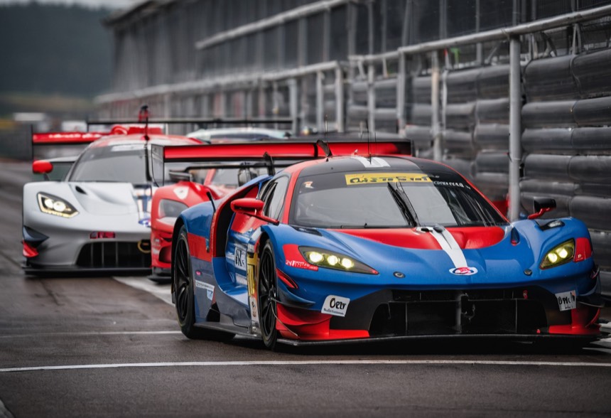 A row of GT3 cars from different manufacturers waiting in the pit lane, a blue and red car nearest the camera.